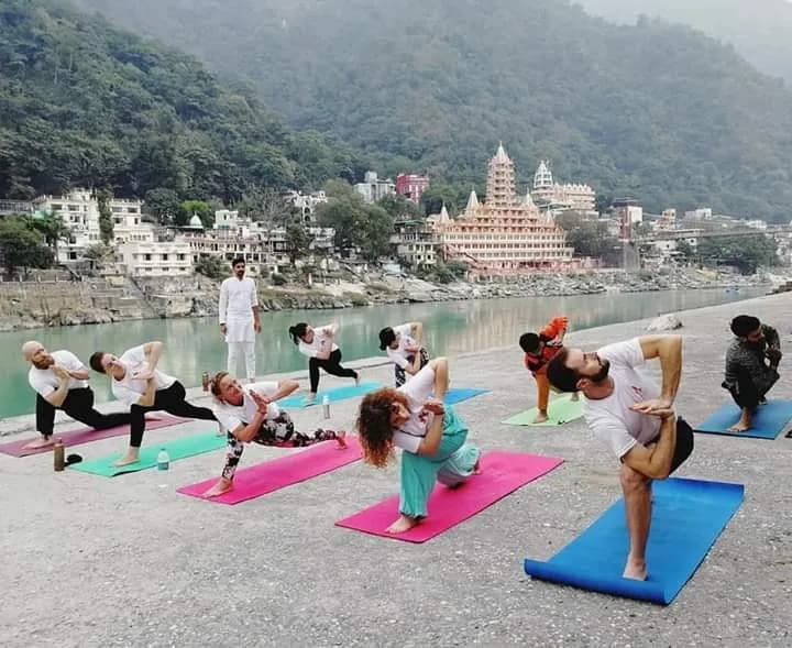 Yoga class practising on the banks of the Ganges with the Rishikesh skyline and temples behind